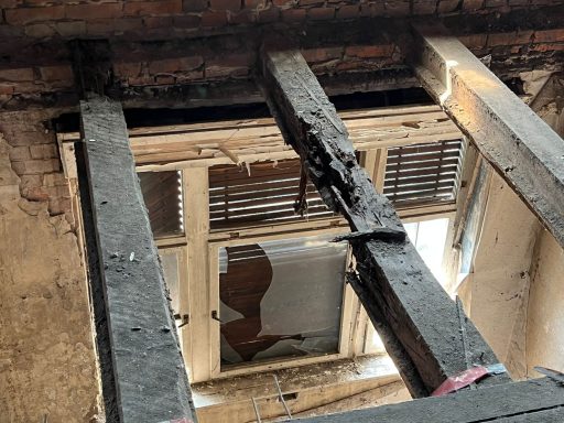 Detailaufnahme der stark beschädigten Deckenbalken in einem denkmalgeschützten Gebäude in Wittenberge, mit sichtbarer Fäulnis und Substanz